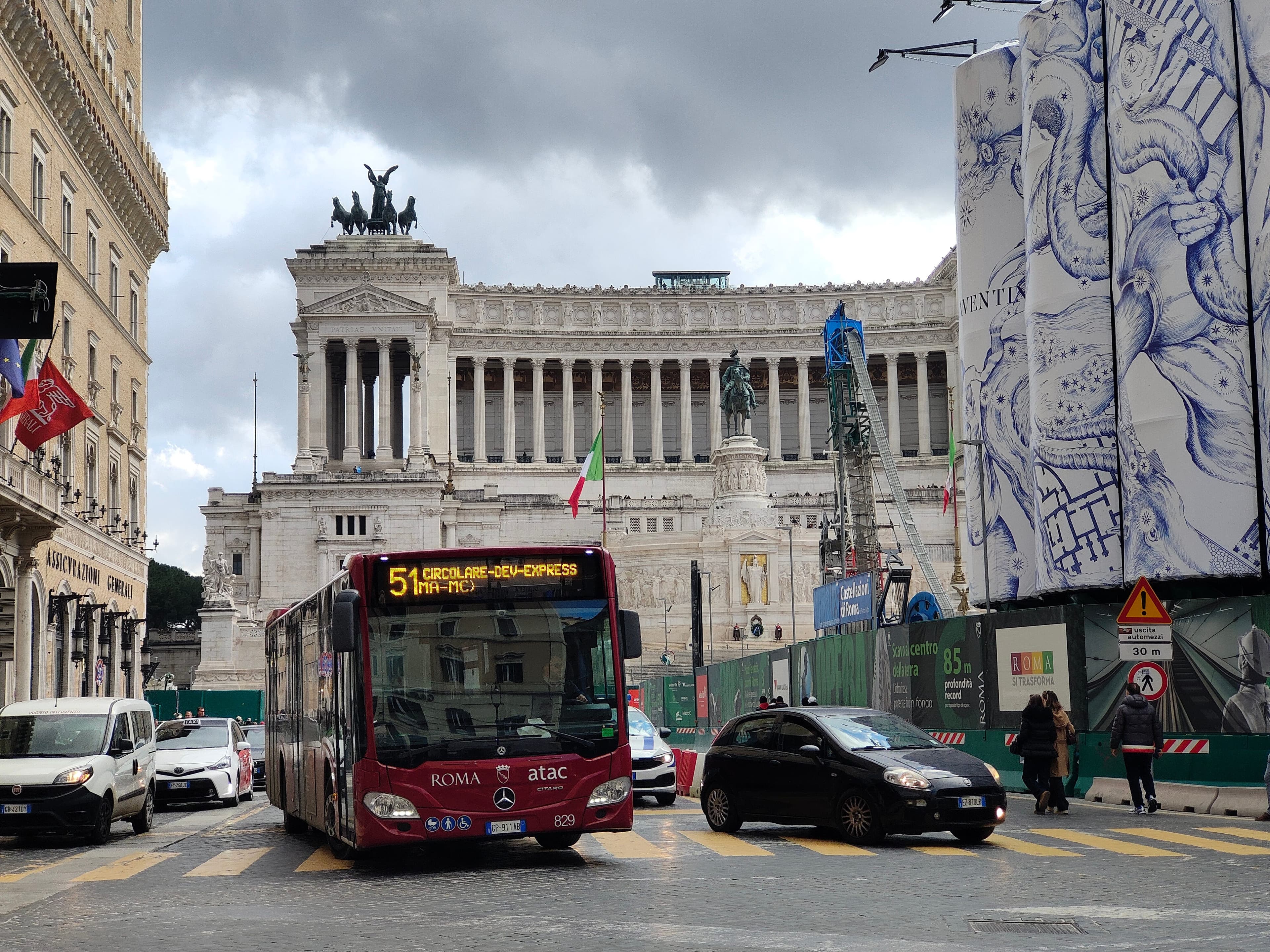 Pedestrians and a red city bus sharing a narrow cobblestone street near Piazza Venezia